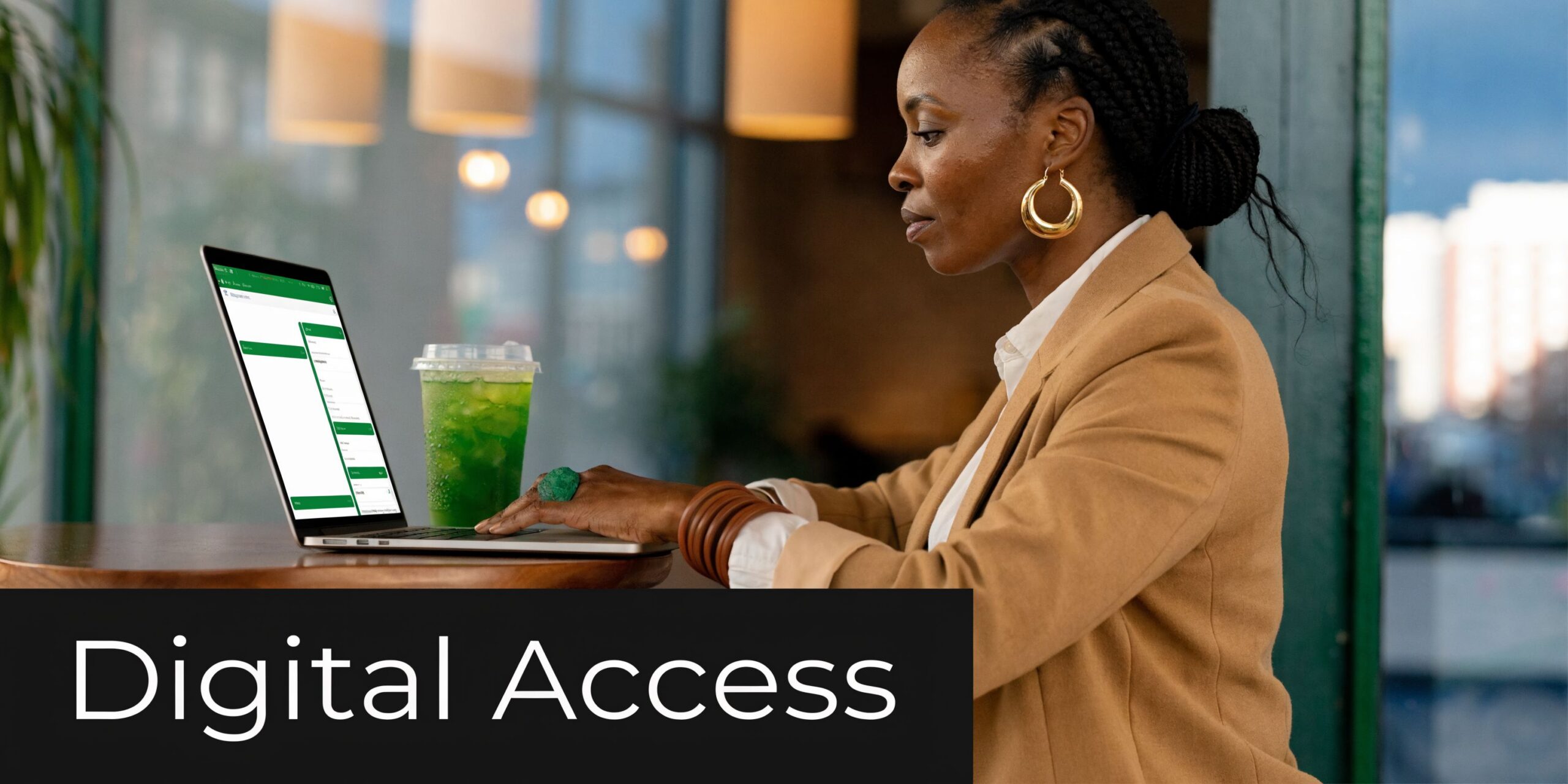 A professional woman in a blazer working on a laptop at a cafe table with green drink.