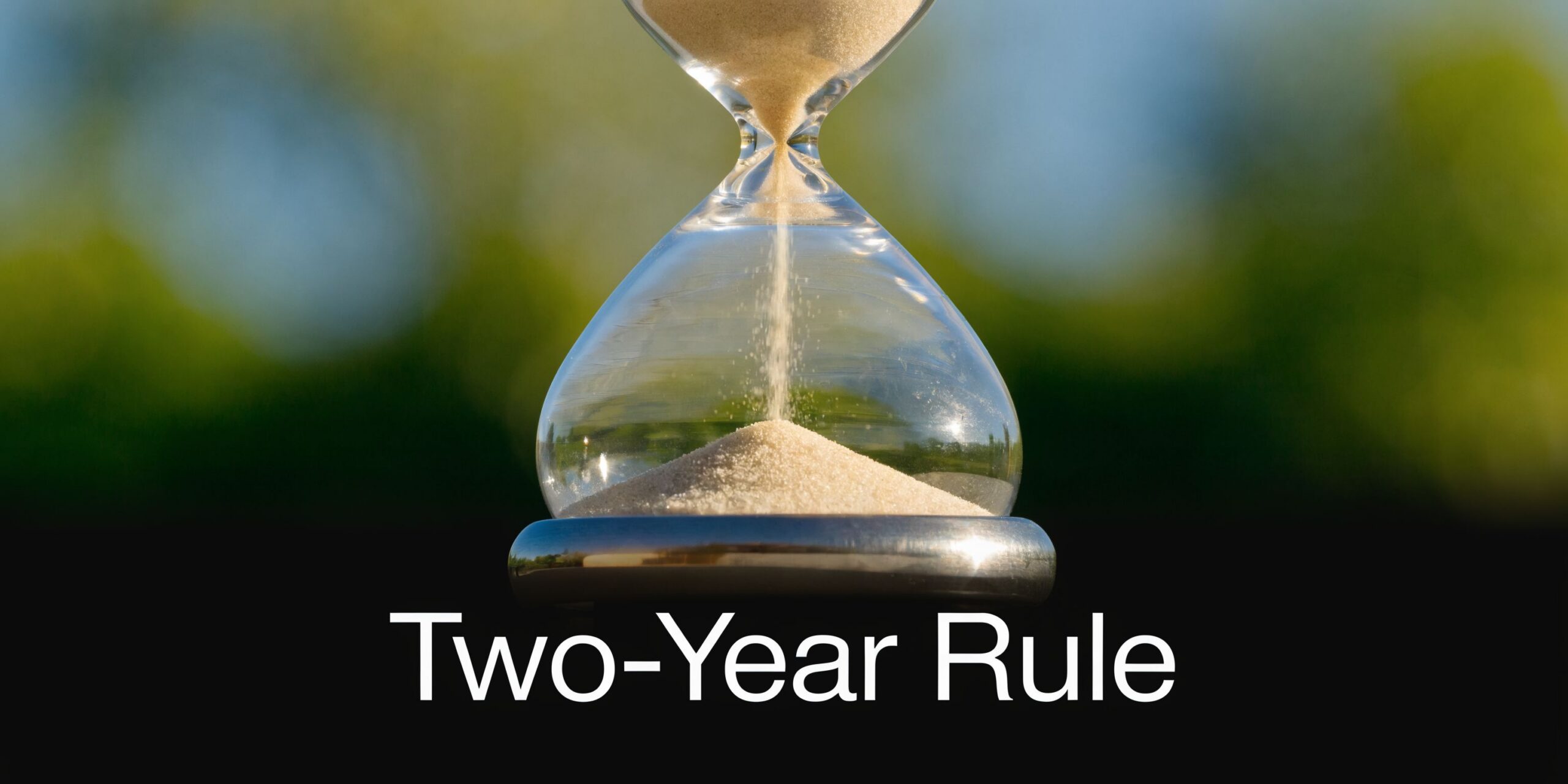 A close-up of an hourglass with sand flowing, symbolizing time and the concept of the two-year rule.