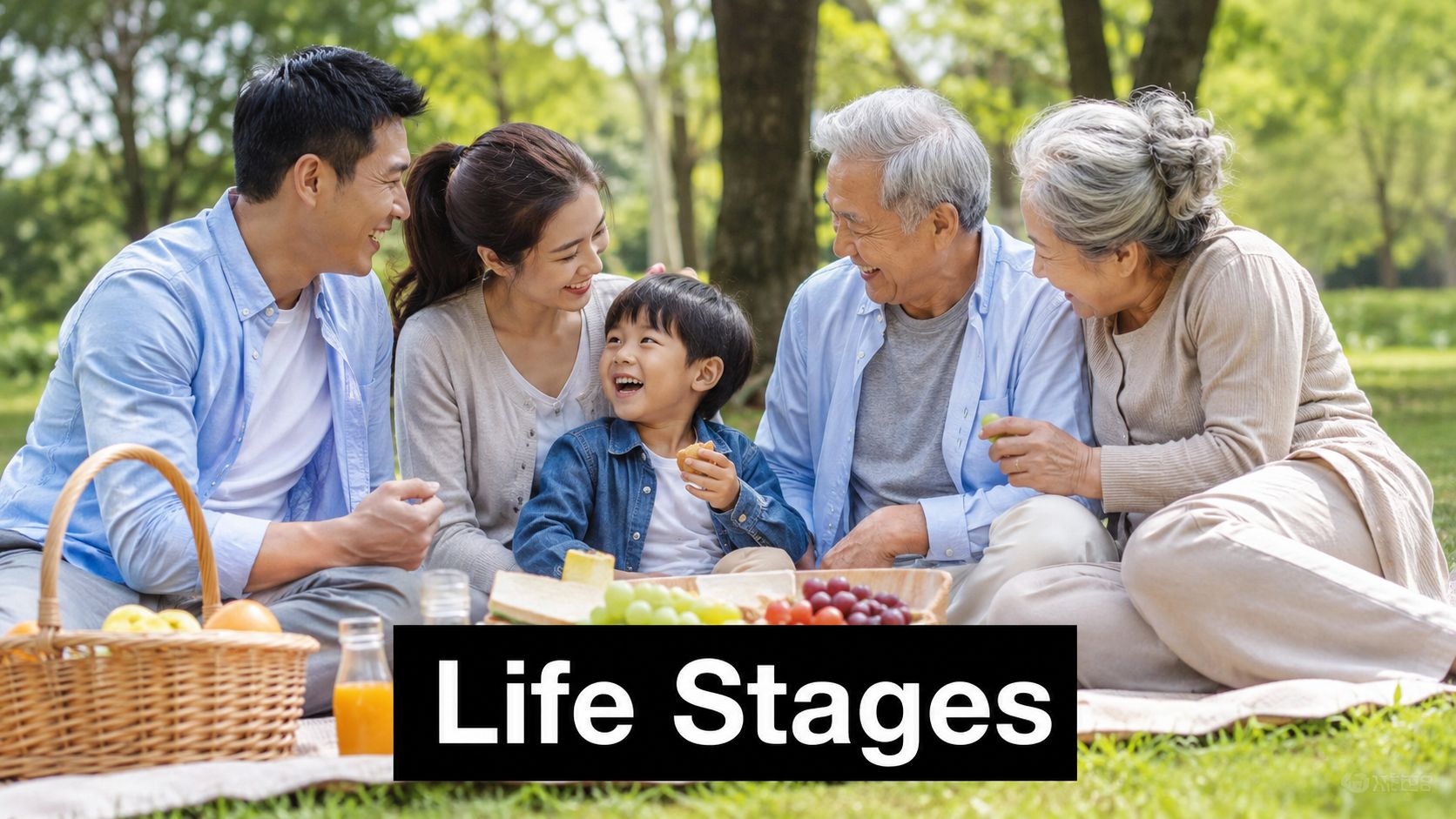 A happy multi-generational family having a picnic in a park with fruit, sandwiches, and juice.