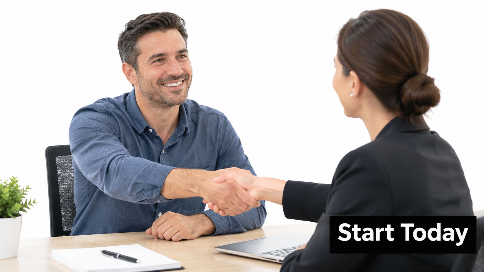 A professional man and woman shake hands across a desk during a business meeting.